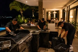 BBQ catering team cleaning the grill and packing equipment after a private evening event at a Cancun villa