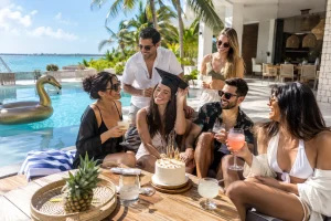 Friends celebrating graduation beside a private villa pool in Cancún with cake and cocktails